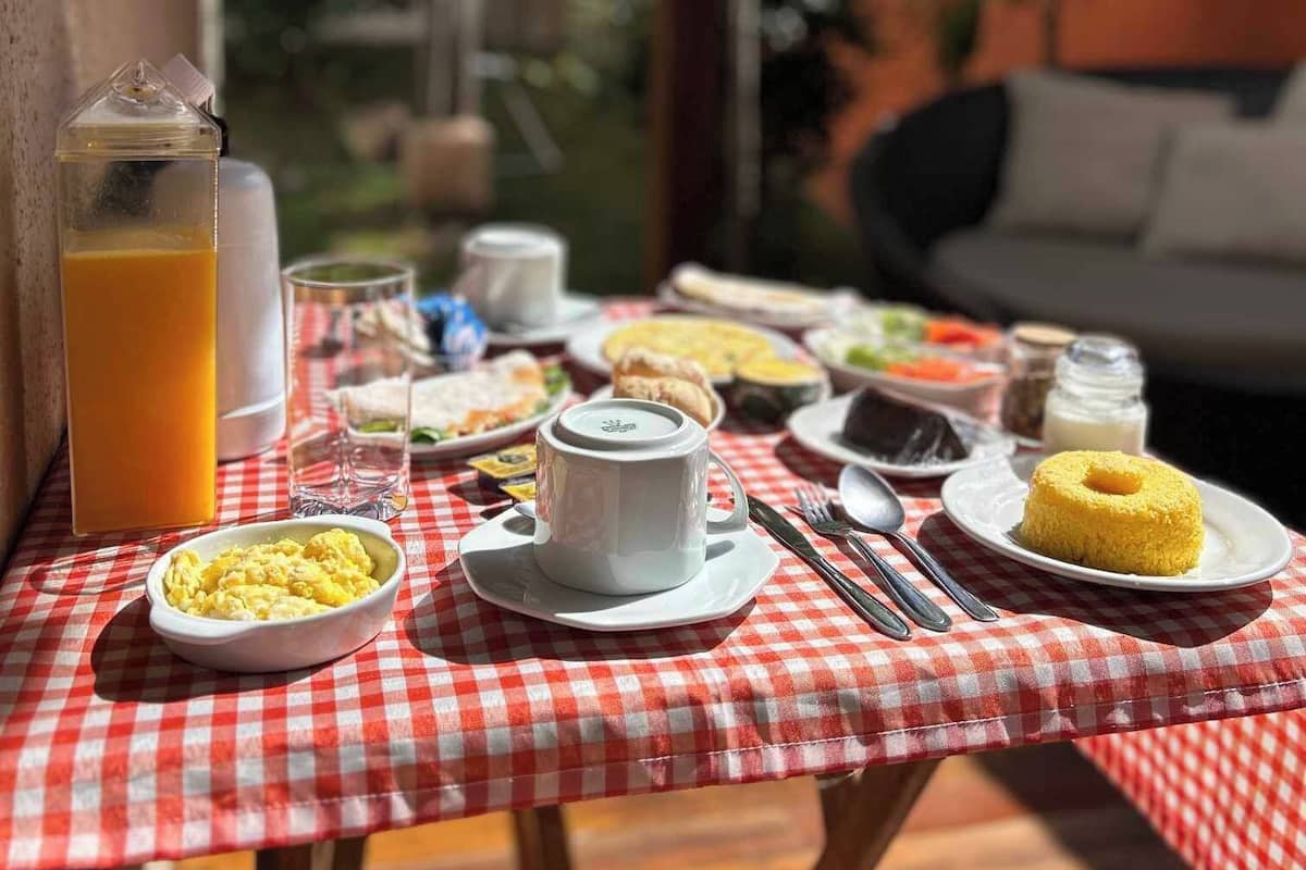 Ein Frühstückstisch im Freien mit karierter Tischdecke, verschiedenen Frühstücksleckereien und einem Glas Orangensaft.