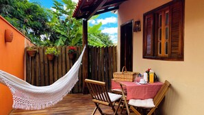 A cozy outdoor seating area with a hammock, wooden chairs, and a table set for two. - Vila Bonita Guest House (Alto Paraíso de Goiás)