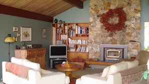 A cozy living room with two white sofas, a fireplace, a stone wall, and a bookshelf filled with books. - Waterfront Vacation Home -only for longer term stays(please contact for details) (Sechelt)