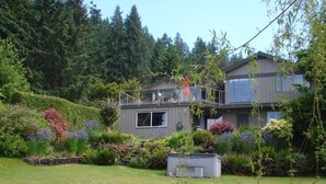 A two-story house with a balcony, surrounded by lush greenery and a variety of plants. - Waterfront Vacation Home -only for longer term stays(please contact for details) (Sechelt)