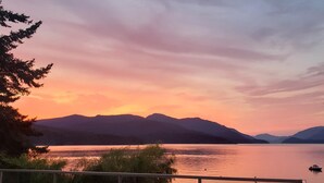 A lakeside view with mountains in the background, a chair, and a railing. - Waterfront Vacation Home -only for longer term stays(please contact for details) (Sechelt)