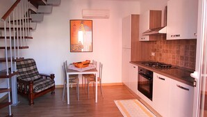 A modern kitchen with white cabinets, a gas stove, and a built-in oven. There is a dining area with a table and chairs, and a staircase with wooden railings. - Casa vacanze La Fonda - Glicine (Santo Stefano di Magra)