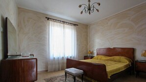 A bedroom with a bed, a nightstand, a dresser, a mirror, a chandelier, and a window with curtains. - Casa vacanze La Fonda - Mimosa (Santo Stefano di Magra)