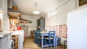 Een keuken met een wasmachine, een tafel met stoelen, een hangende kruidenrek en een koelkast.