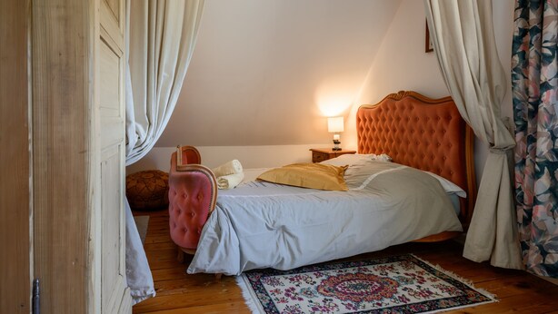 Een slaapkamer met een bed, nachtkastje, lamp, raam met gordijnen en een houten vloer.