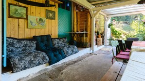 Een overdekte veranda met een houten bank, een tafel en stoelen.