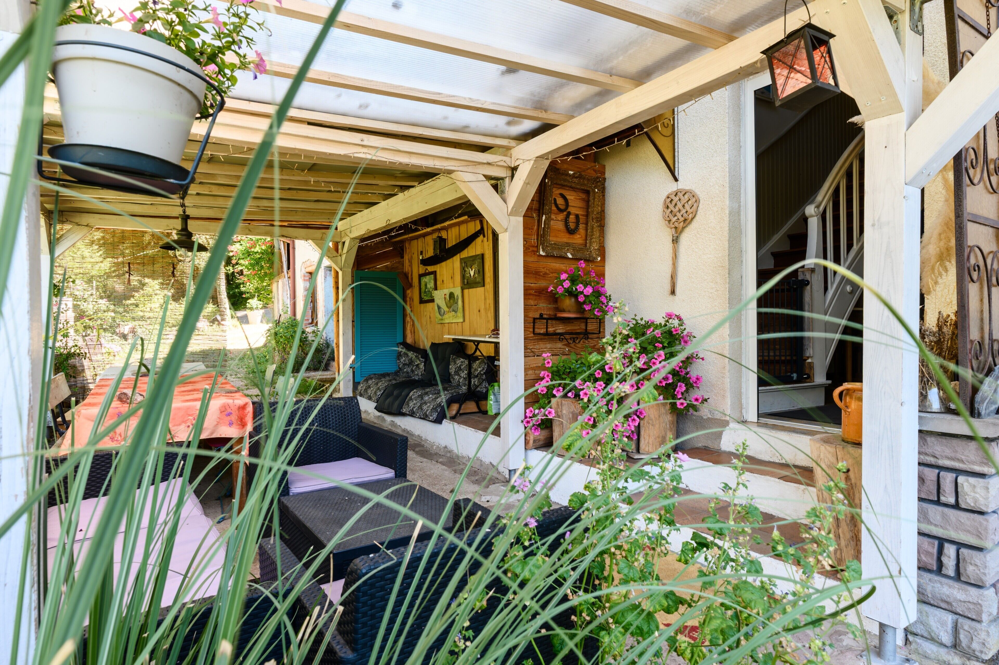 A covered outdoor seating area with wicker furniture, a hanging planter, and a wooden door with a heart-shaped decoration.