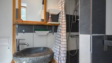 Une salle de bain avec un lavabo en pierre, une étagère en bois, un miroir, un rideau de douche et un porte-serviettes.