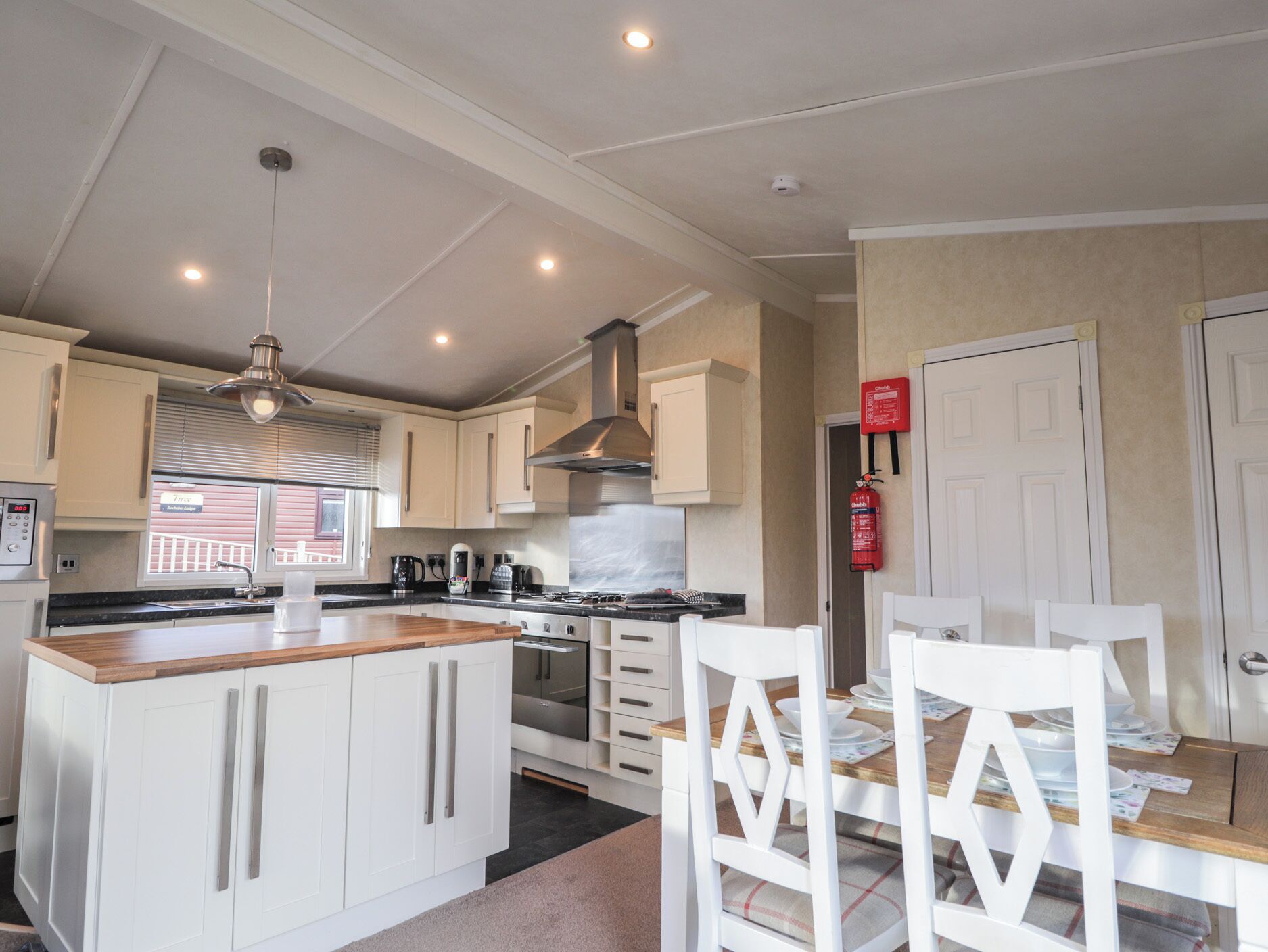 A modern kitchen with white cabinets, a wooden countertop, and a dining area with white chairs.