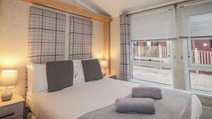 Habitación de hotel con una cama grande, dos lámparas de noche, una ventana con persianas y vista a un edificio.
