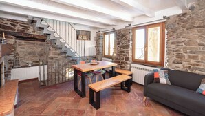 Ein gemütliches Interieur mit einer Steinwand, einer Holztreppe, einem Esstisch mit Bänken und einer Couch.