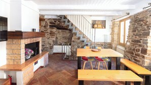 Ein gemütliches Interieur mit Kamin aus Stein, Holzboden, einer Essecke mit Bänken und einer Treppe zu einer oberen Ebene.