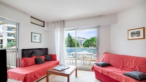 A room with a bed, a sofa, a coffee table, and a balcony with a view of buildings and trees. - Le Lido Apartment – Beach, Pool, Parking, Sea View, Wi-Fi, Air Conditioning (Cagnes-sur-Mer)