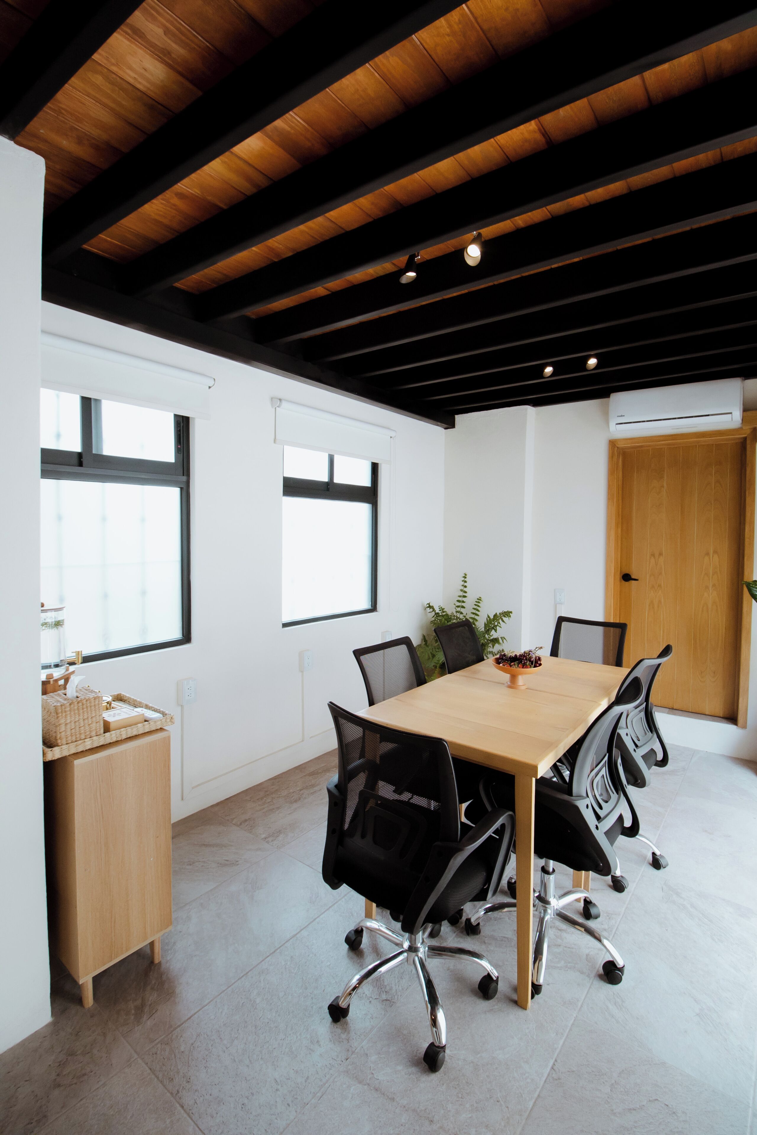 A conference room with a wooden table, black chairs, a potted plant, and a wooden cabinet.
