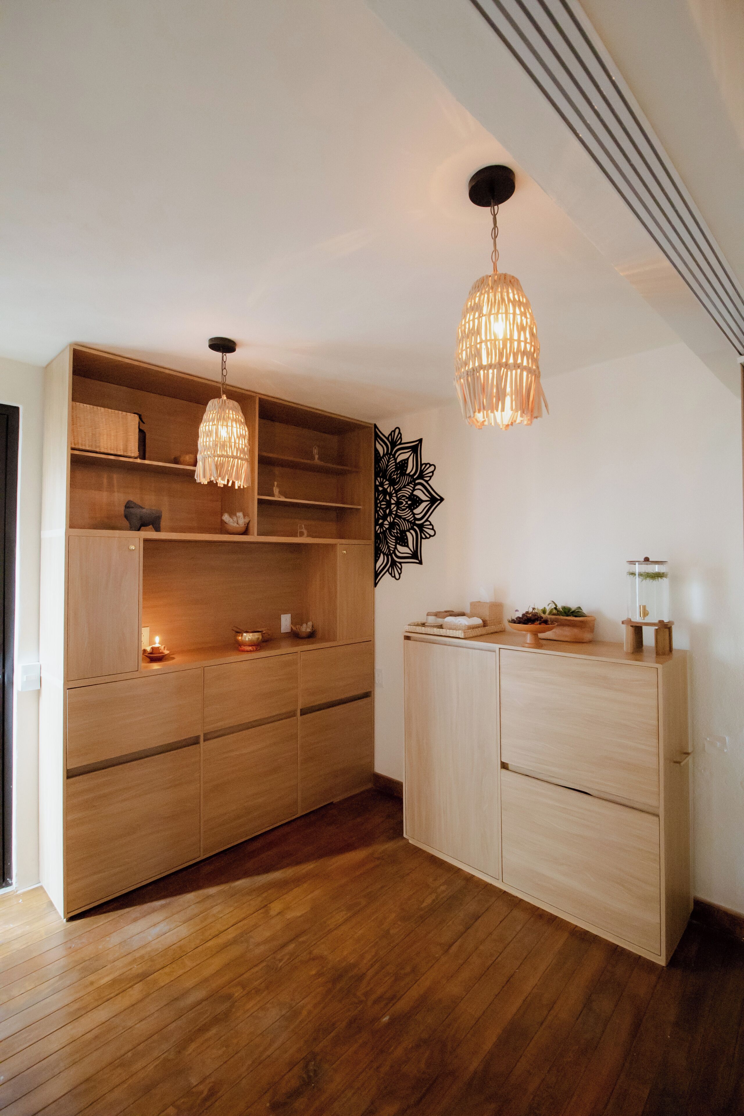 A modern room with wooden cabinetry, a decorative wall piece, and two hanging light fixtures.
