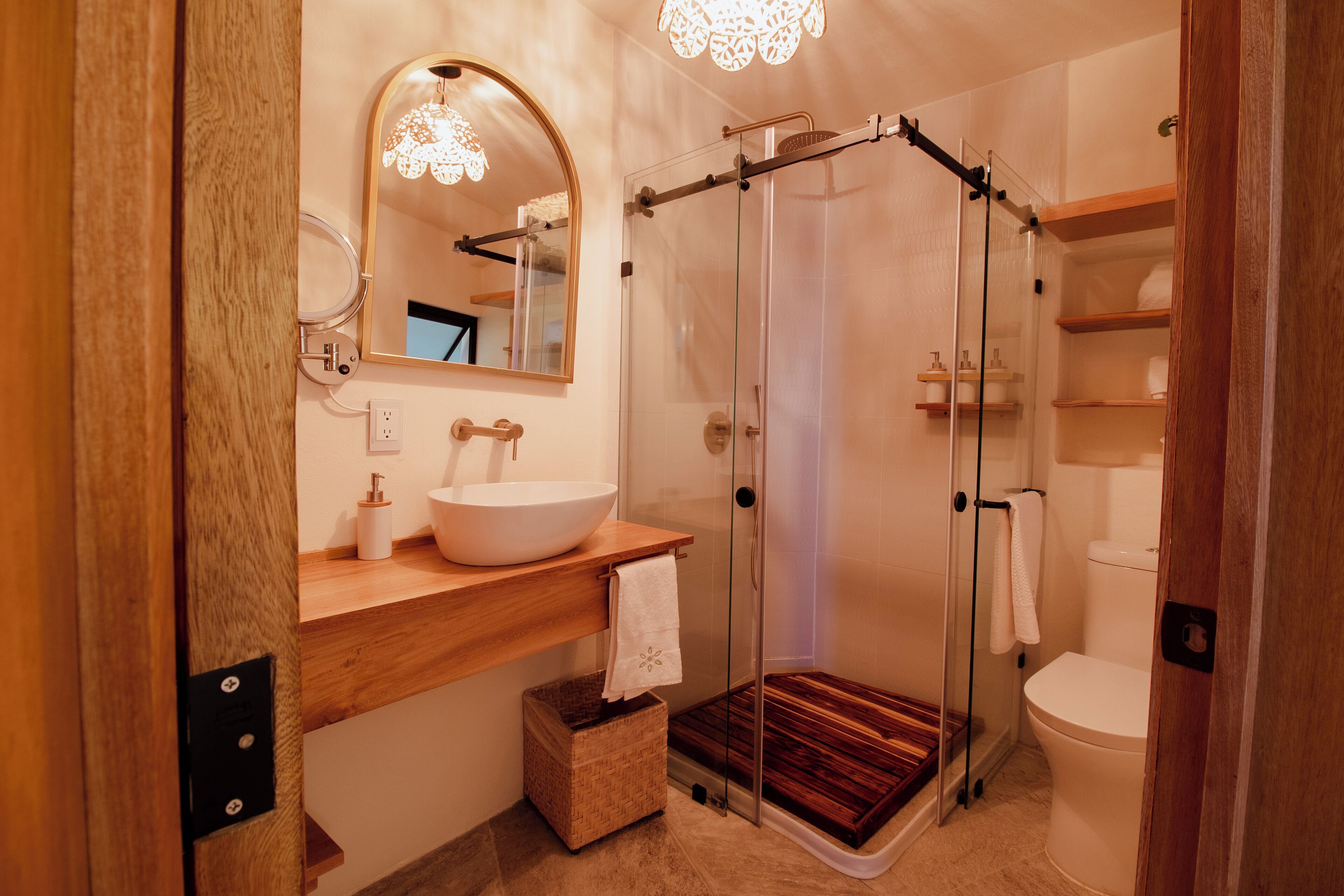 A modern bathroom with a wooden vanity, a large mirror, a glass shower enclosure, and a toilet.