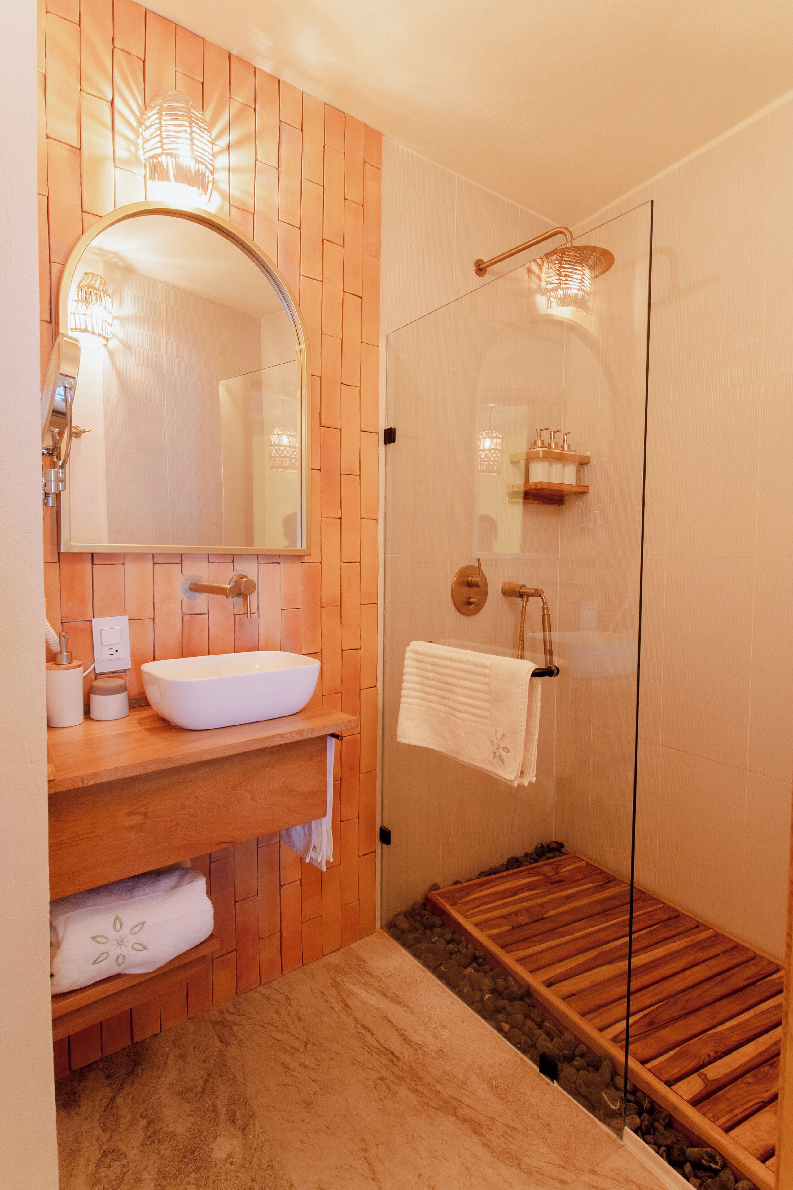 A bathroom with a wooden vanity, a large mirror, a glass shower enclosure, and a wooden bath mat.