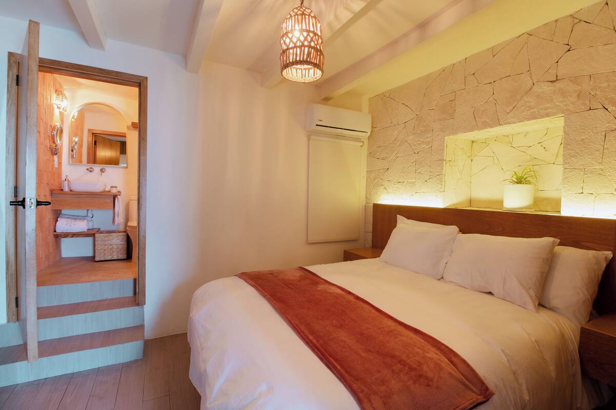 Ein Schlafzimmer mit einem großen Bett, einem Holz-Kopfteil, einer Steinwand und einer kleinen Pflanze.
