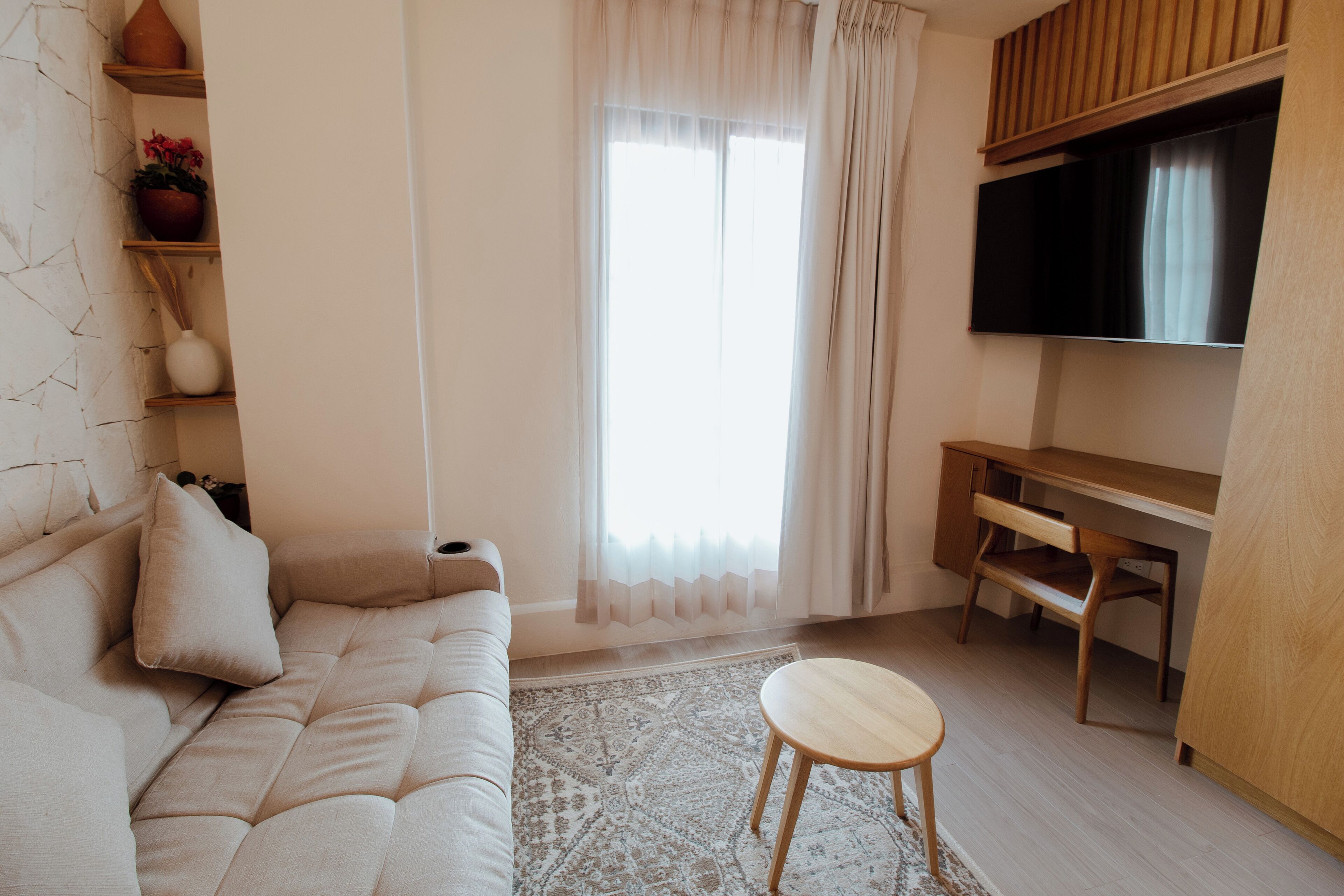 Una sala moderna con un sofá, una mesita redonda, un televisor y un escritorio de madera.