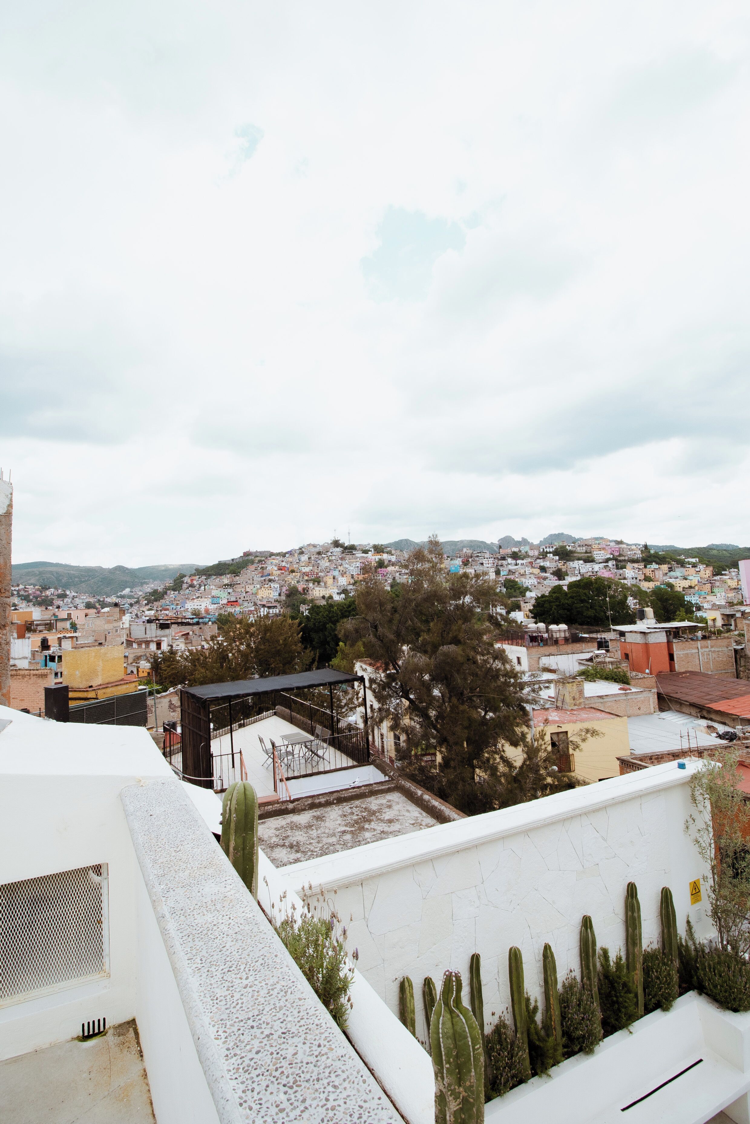 A rooftop terrace with a view of a densely built cityscape, including a variety of buildings and a distant hill.
