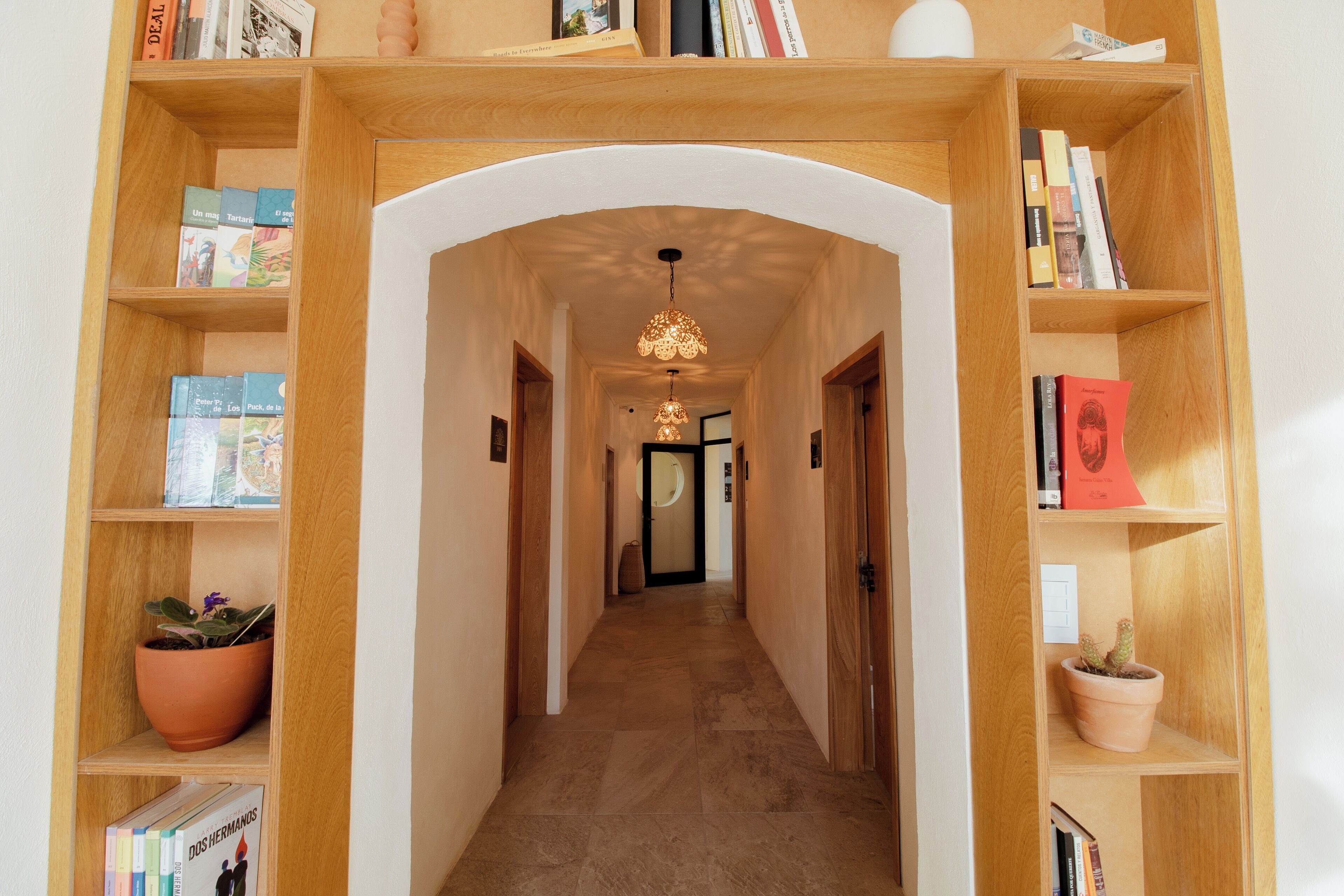 Un pasillo con estanterías de madera a ambos lados, un arco central y una lámpara colgante.