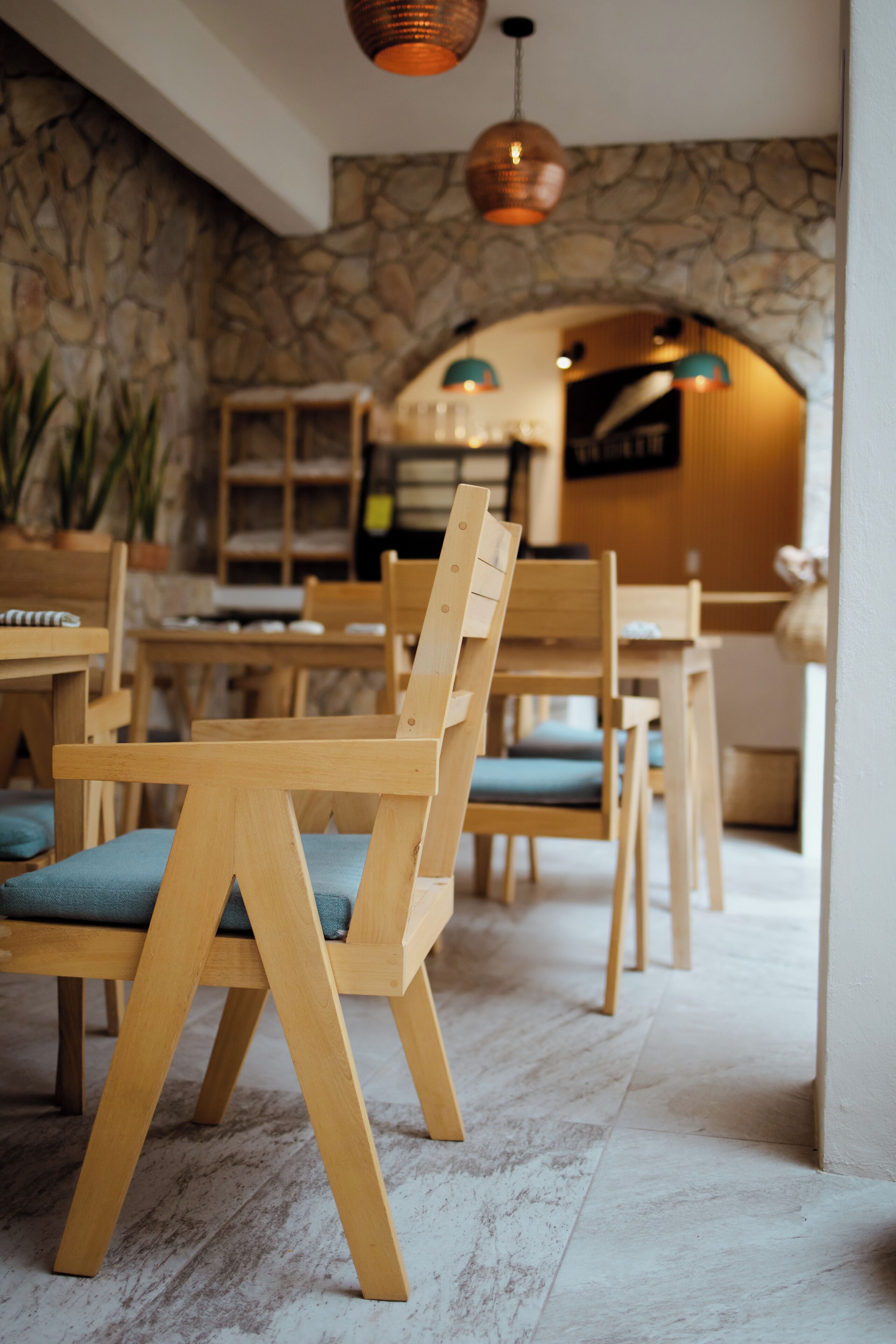 A wooden dining area with chairs and tables, stone walls, and hanging pendant lights.