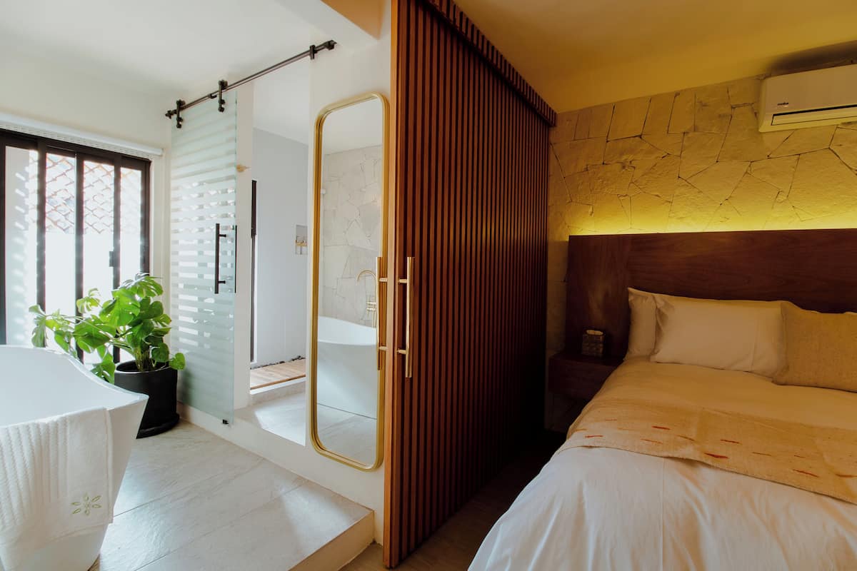 Ein modernes Hotelzimmer mit einem großen Bett, einem Holzschrank, einem Badezimmer mit Glastür und einer Topfpflanze.