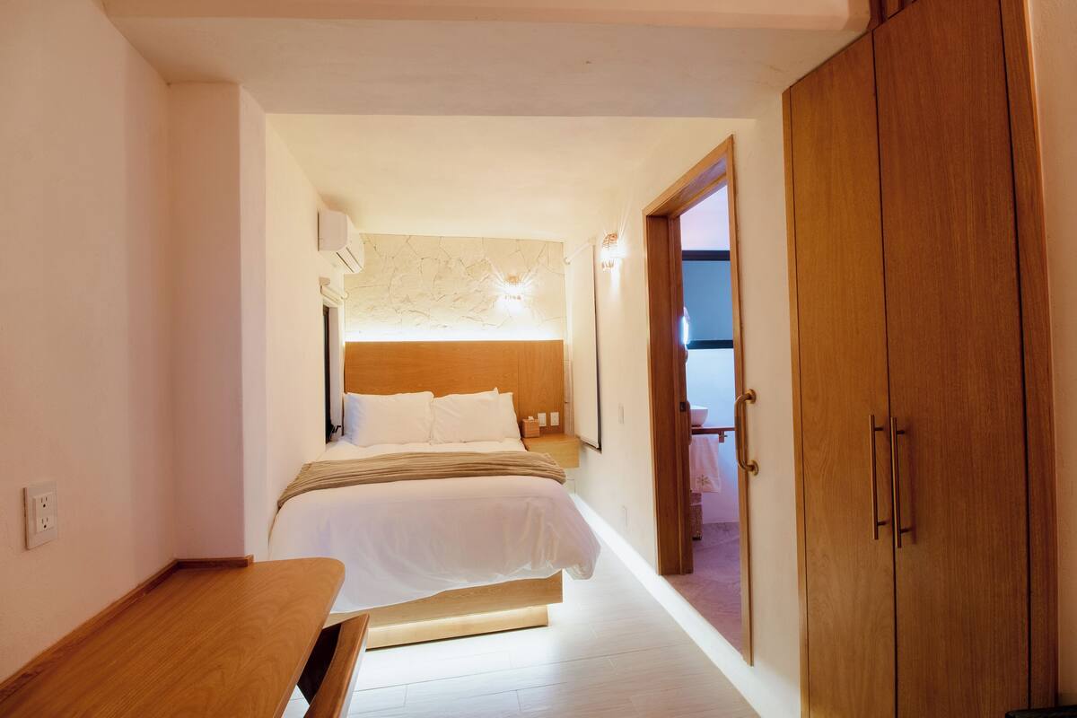 Ein Schlafzimmer mit Bett, Nachttisch, Kleiderschrank und Blick ins Freie.