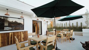 An outdoor seating area with wooden tables and chairs, a large umbrella, and a cactus garden in the background. - Bernardino Hotel Boutique (Guanajuato)