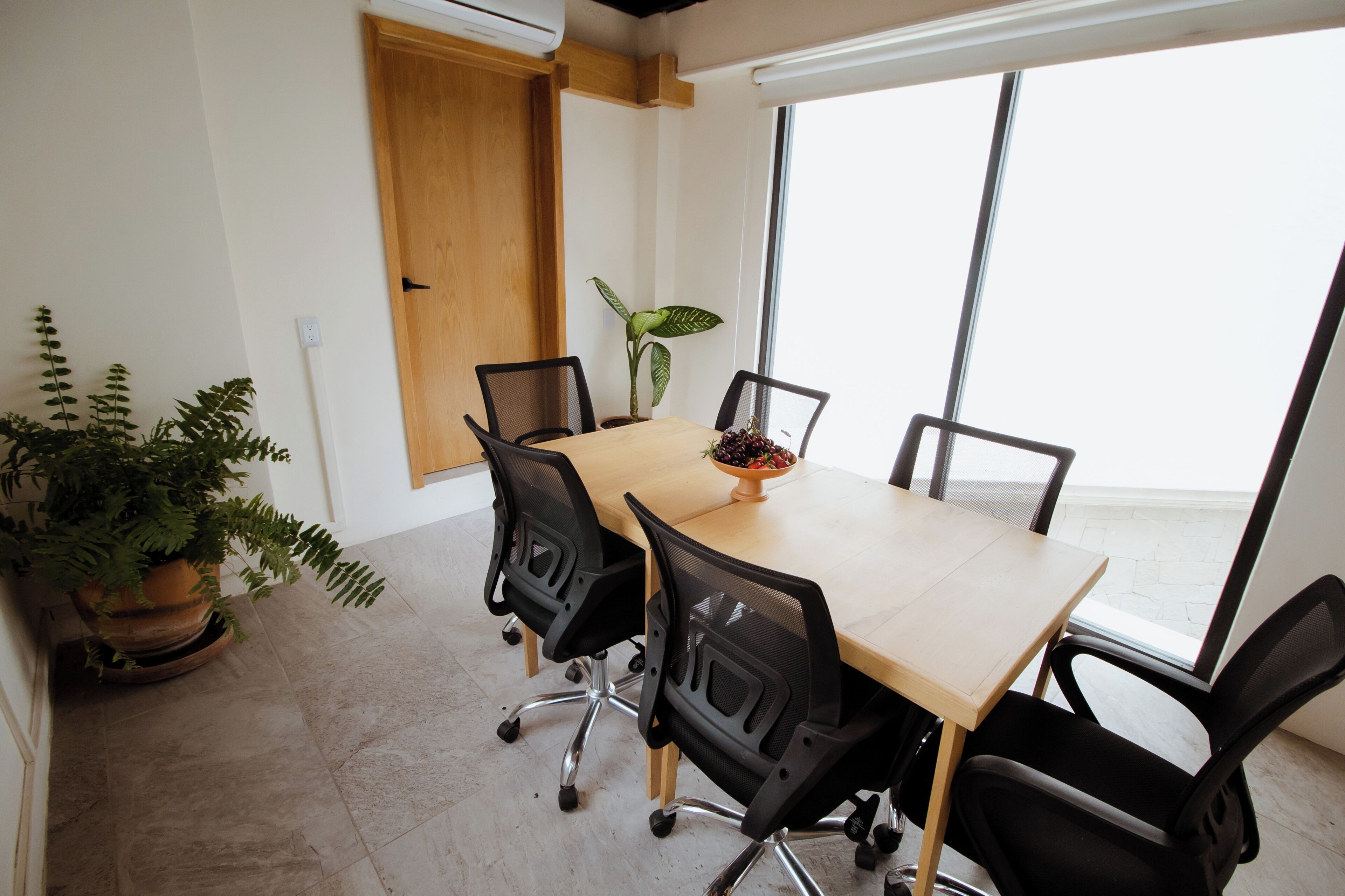 Uma sala de conferências com uma mesa de madeira, cadeiras pretas, uma planta em vaso e uma cesta de frutas.
