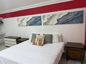 Een slaapkamer met een bed, twee nachtkastjes, een dressoir en twee abstracte schilderijen aan de muur.