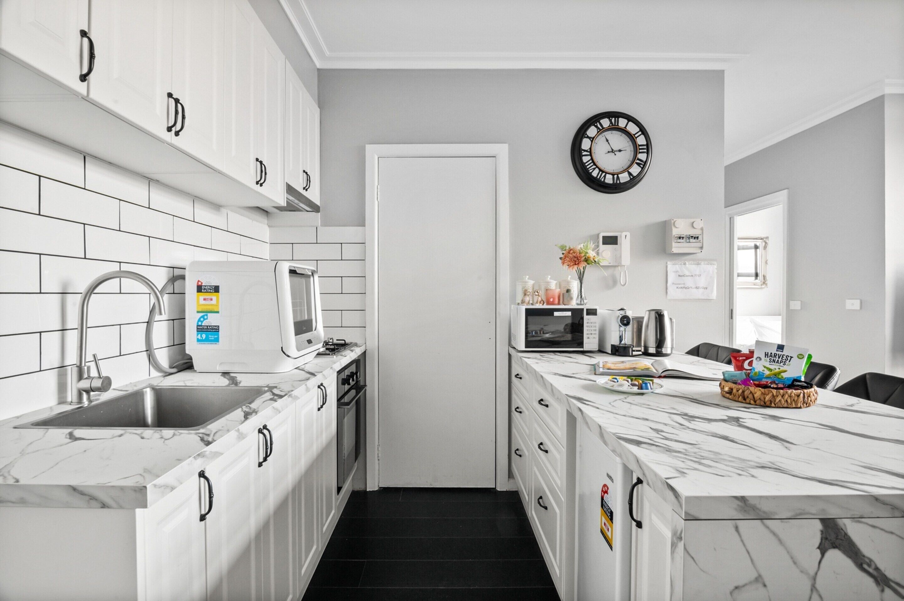 A modern kitchen with white cabinets, a marble countertop, a built-in microwave, and a clock on the wall.