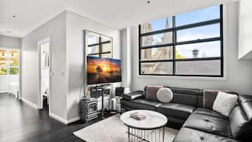 A modern living room with a black leather sofa, a white coffee table, and a large window with a view of a building.