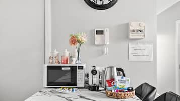 A modern kitchen with a microwave, coffee maker, and a basket of snacks on a marble countertop.