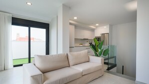 Ein modernes Wohnzimmer mit einem beige gefärbten Sofa, einer Glastreppe und einer Küche im Hintergrund.