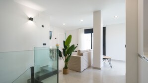 Ein modernes Interieur mit Glastrennwand, einer Treppe, einer Wohnbereits mit Sofa und einer Topfpflanze.