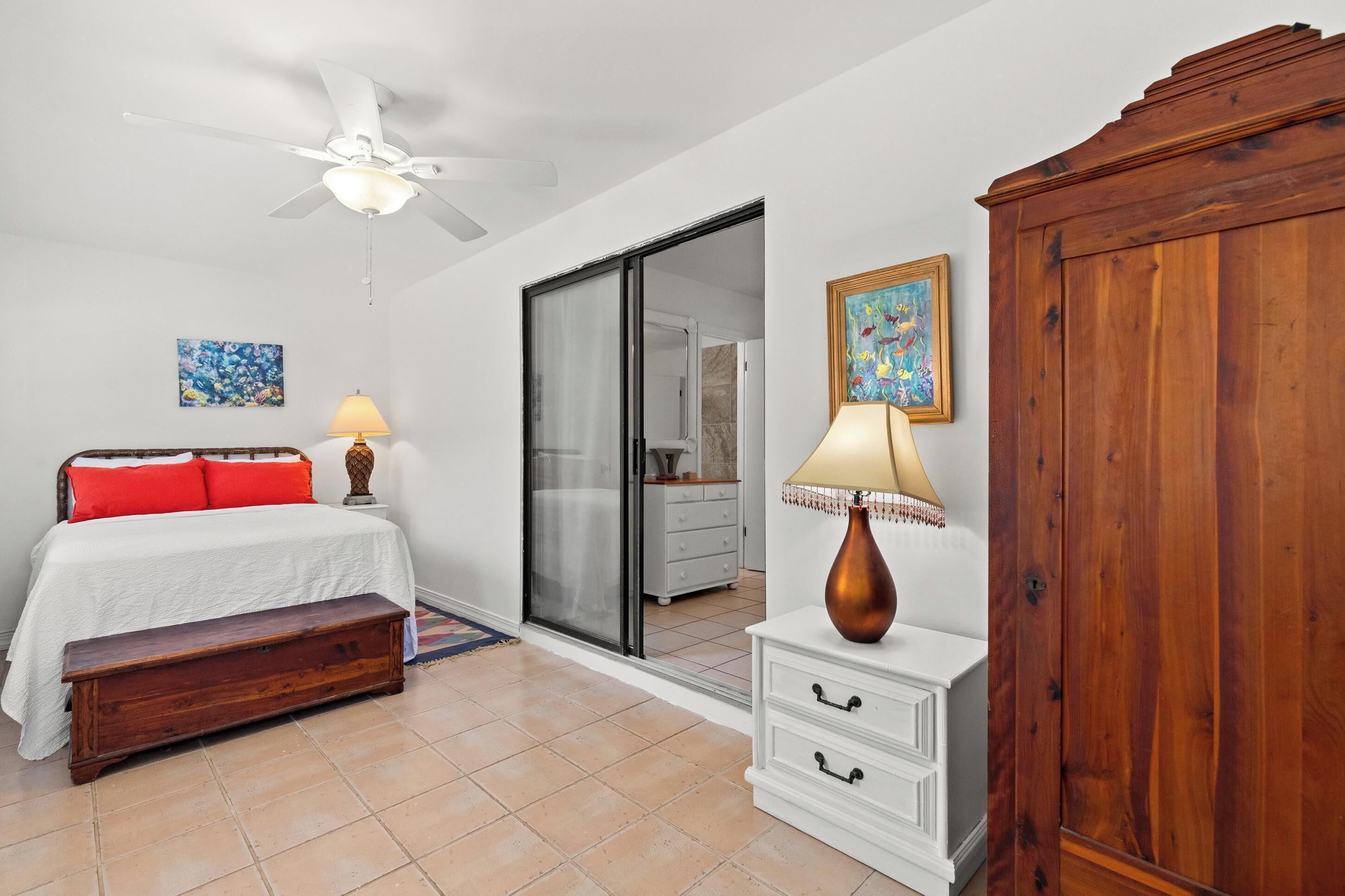 A bedroom with a bed, a nightstand, a wooden cabinet, a ceiling fan, and a sliding glass door leading to a bathroom.