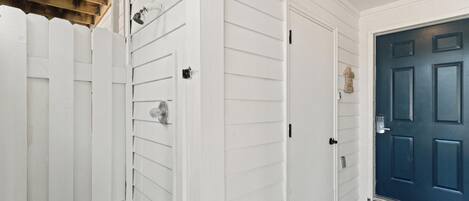 Un pasillo con paredes exteriores blancas, una puerta azul y una valla de piquetes blancos.