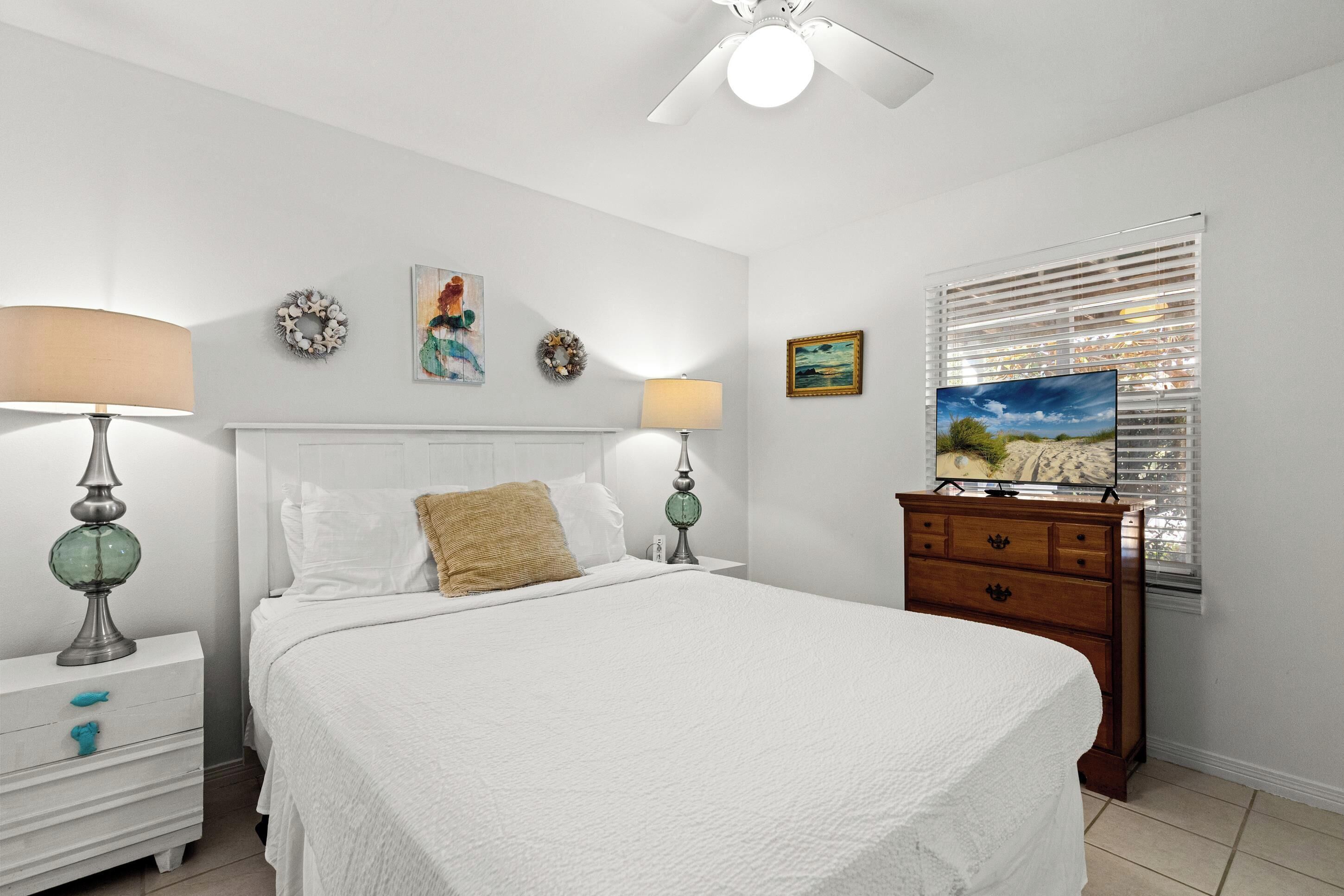 A bedroom with a bed, two bedside tables with lamps, a dresser, and a window with blinds.