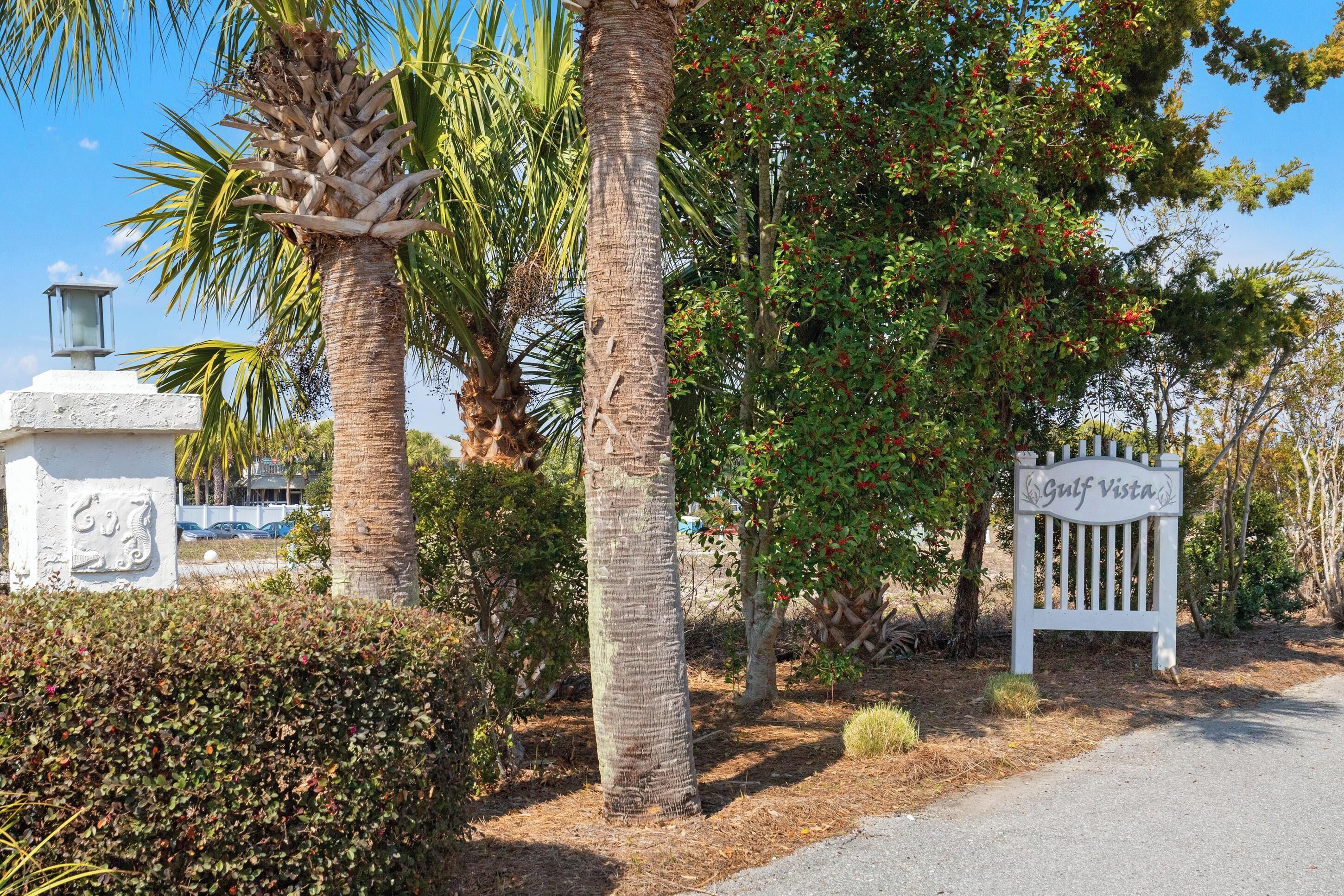 A sign reading "Gulf Vista" with a white bench and palm trees in the background.