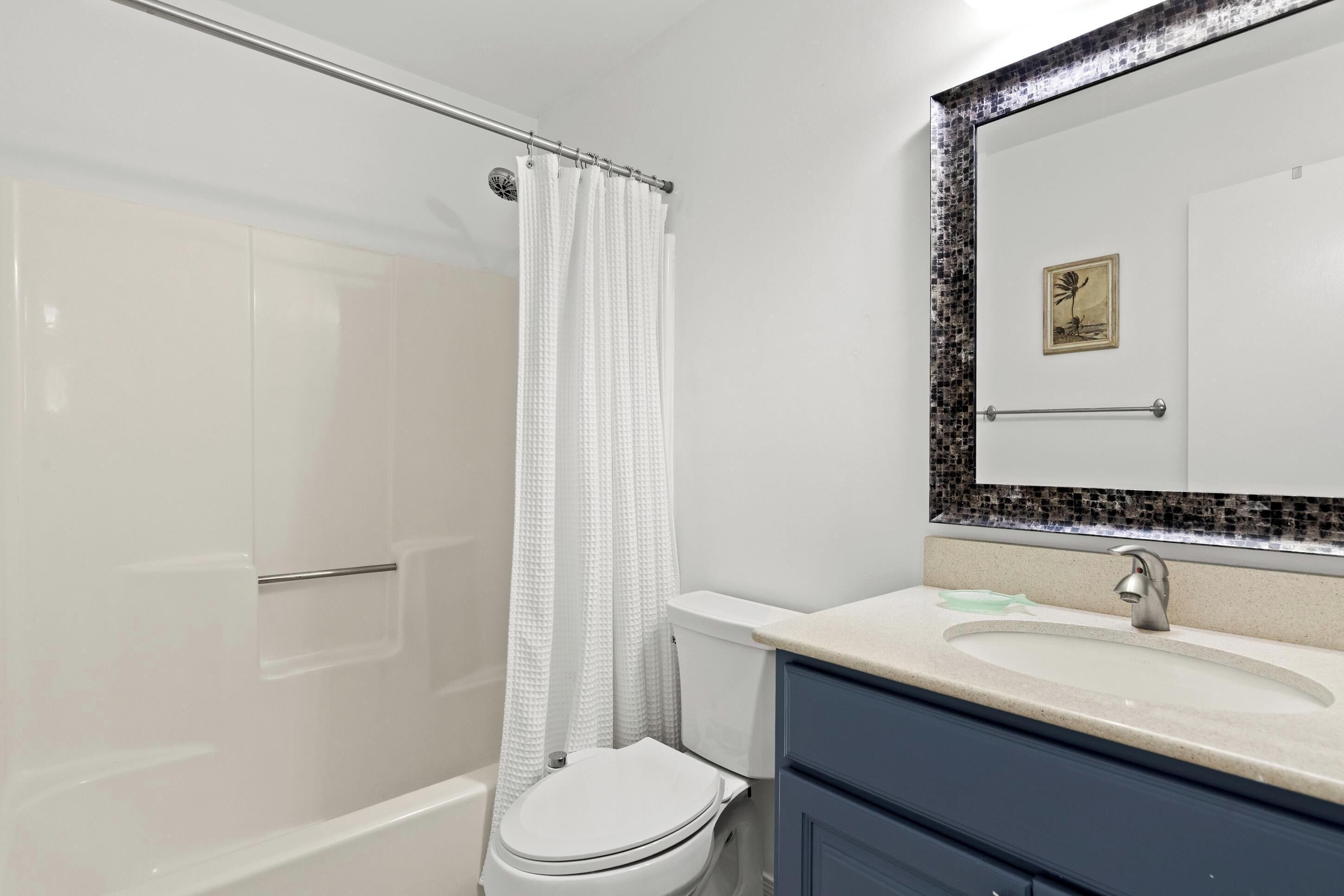 A bathroom with a shower, toilet, sink, and a mirror with a decorative frame.