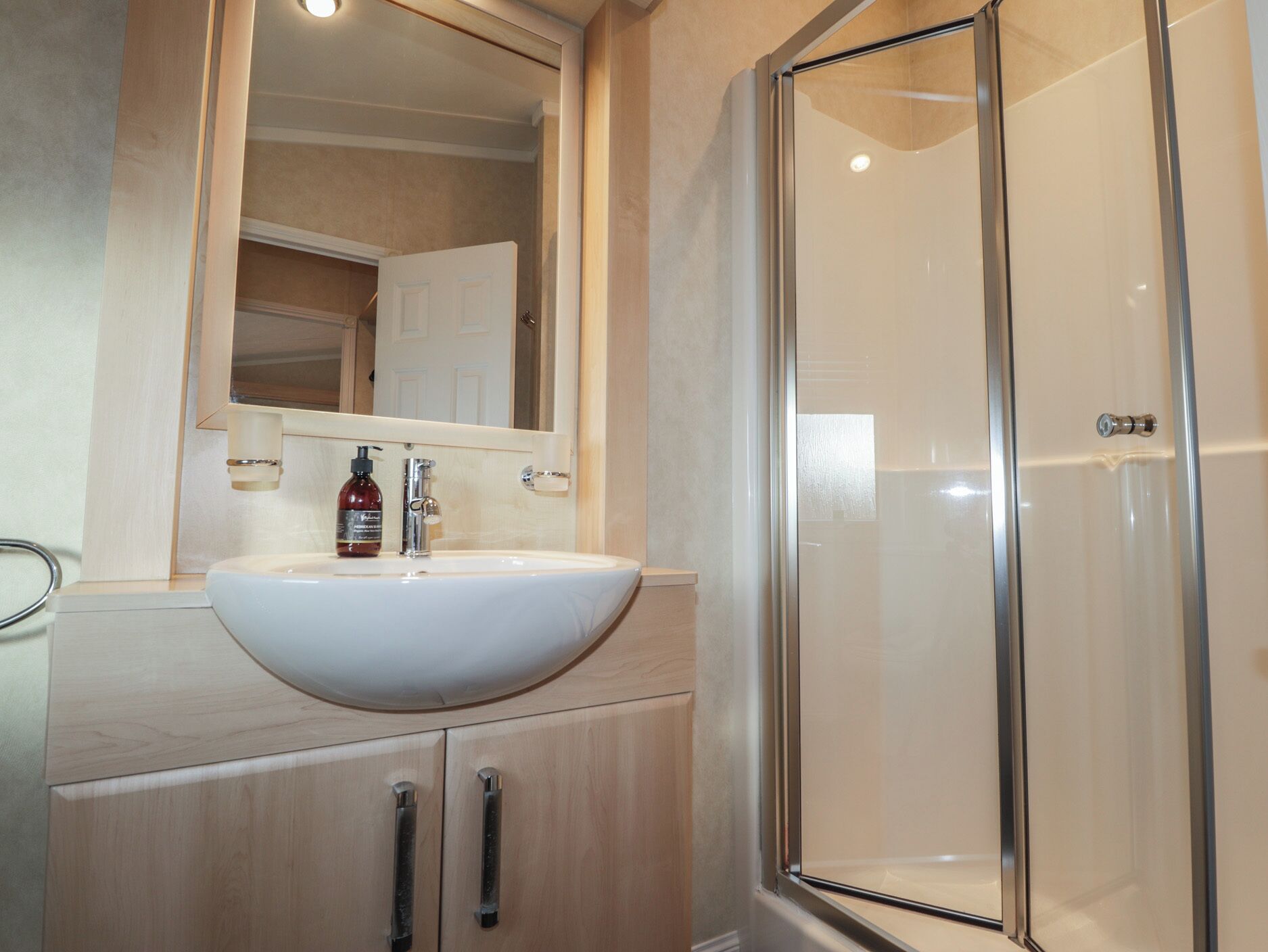 Une salle de bain avec un lavabo blanc, un miroir au-dessus et une cabine de douche en verre.