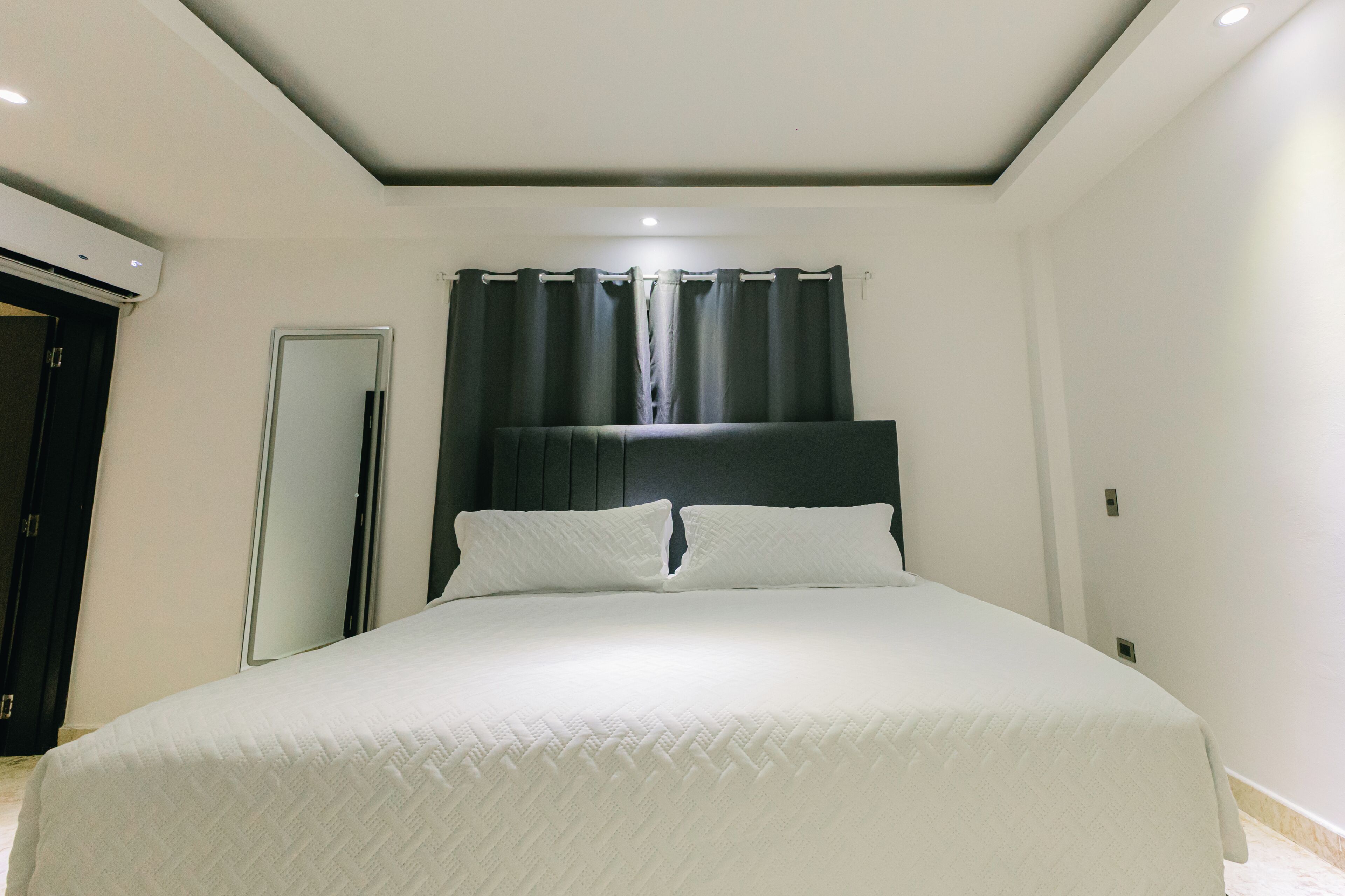 A bedroom with a bed, a door, a mirror, and a window with curtains.