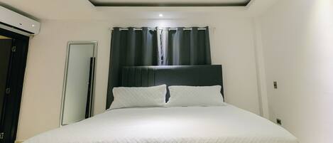 A bedroom with a bed, a door, a mirror, and a window with curtains.