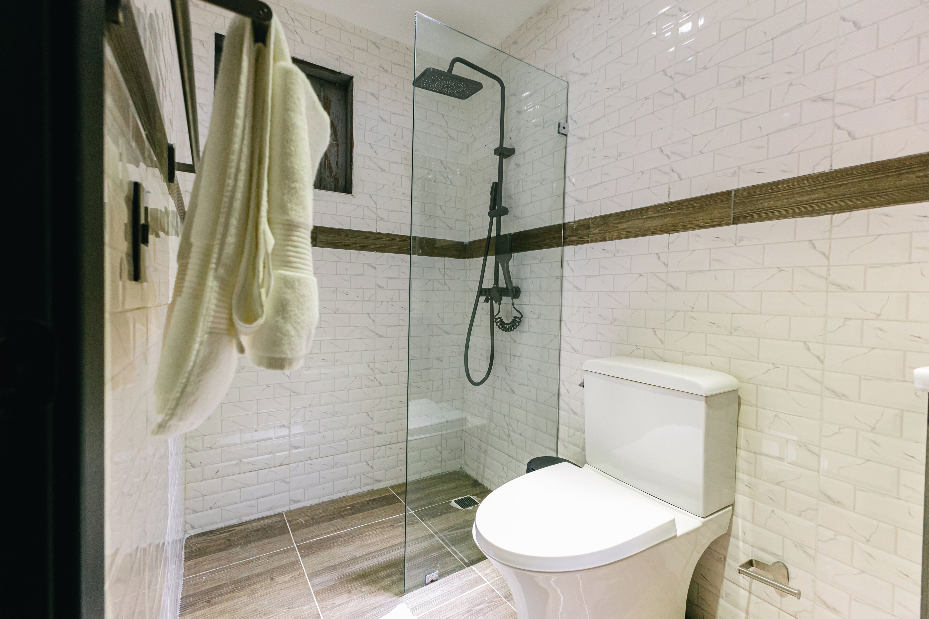 Une salle de bain moderne avec une douche à parois de verre, des toilettes blanches et une bande décorative en bois sur le mur.