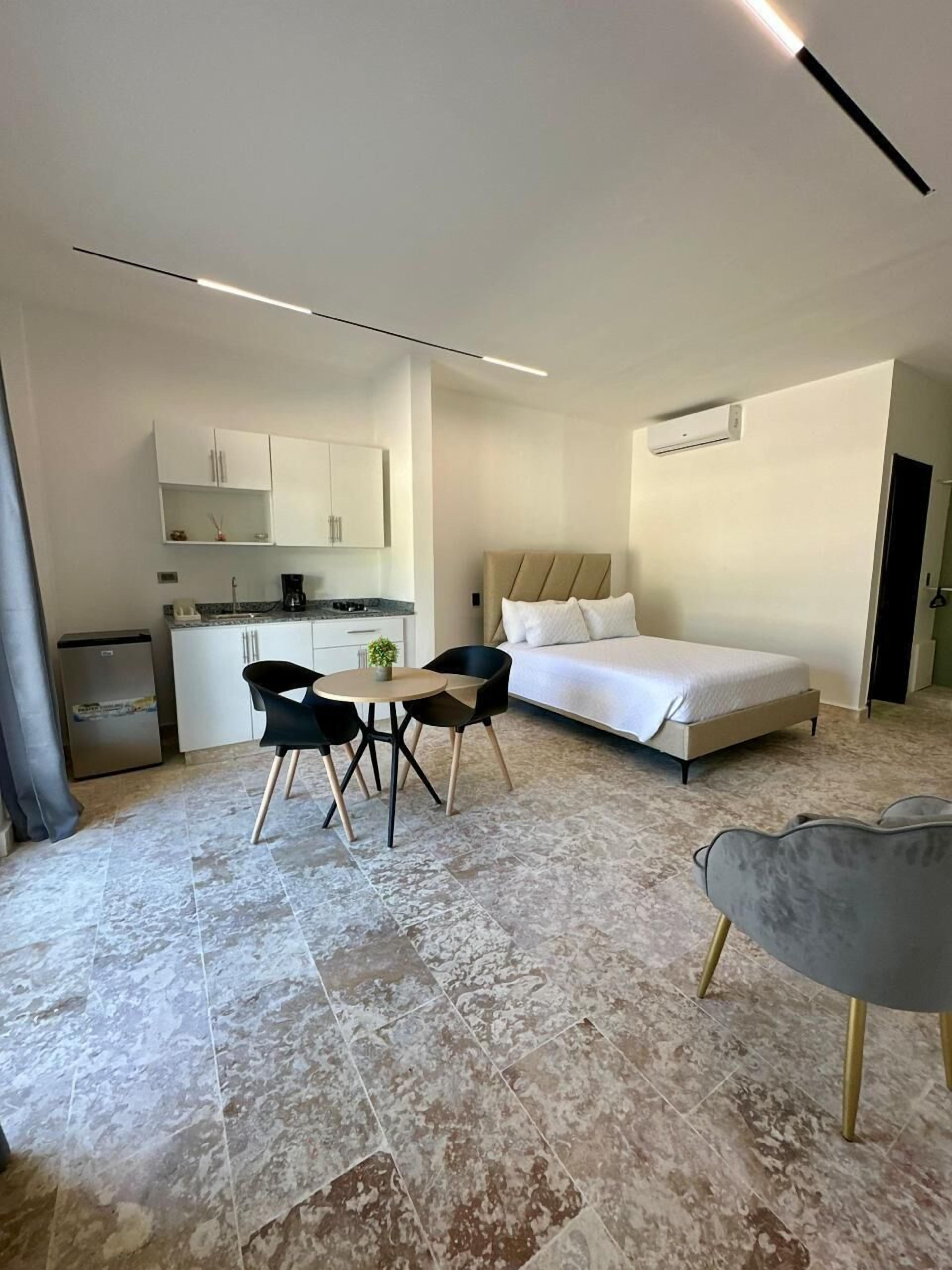 Een moderne hotelkamer met een bed, een klein eettafeltje met stoelen, een kitchenette en een badkamer.