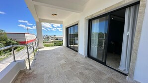 En balkon med flisegulv, gelænder i metal og store skydedøre til et overdækket område.
