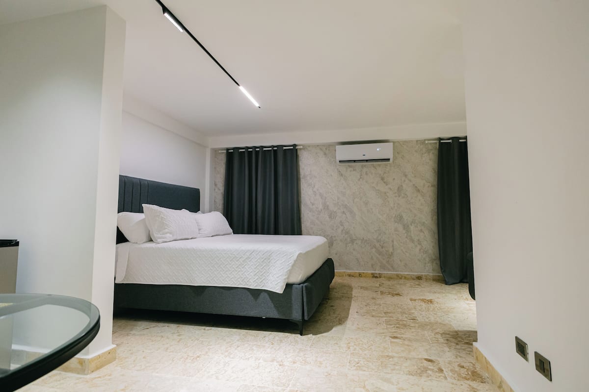 A modern bedroom with a bed, a glass table, and a marble floor.