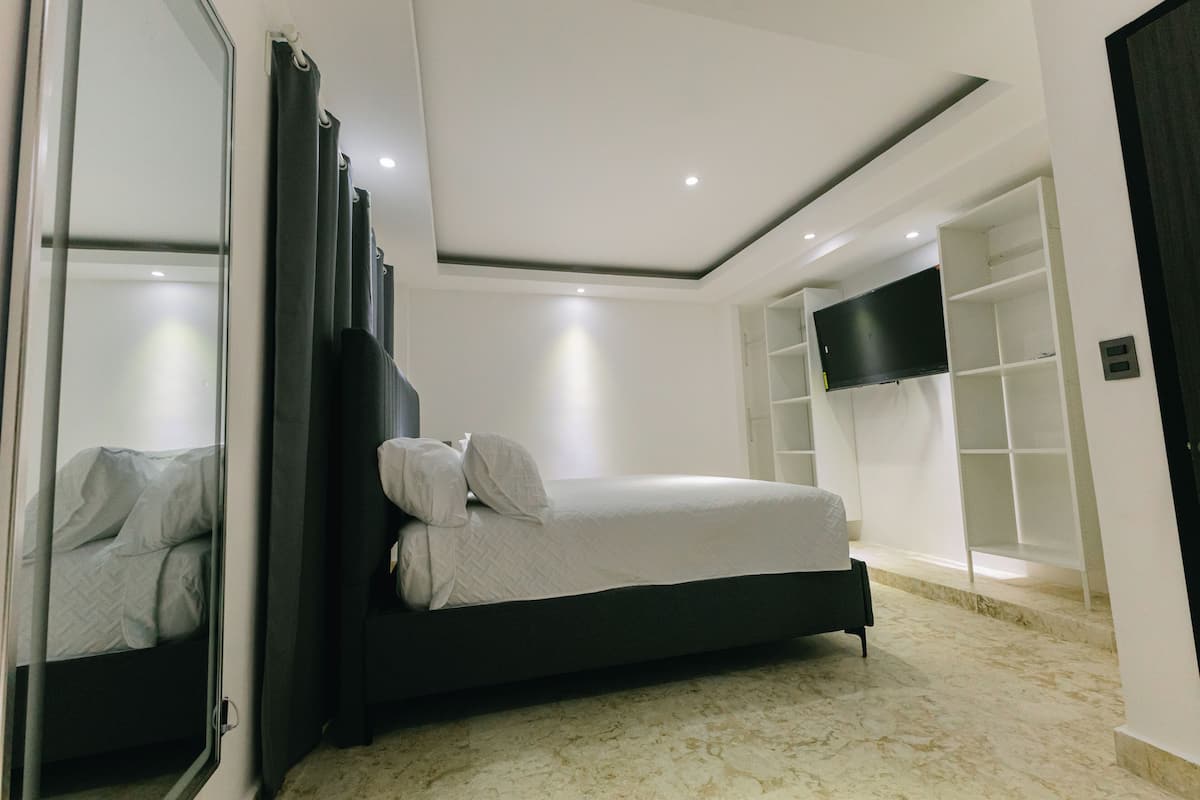 A modern bedroom with a bed, a large mirror, a TV, and built-in shelving.
