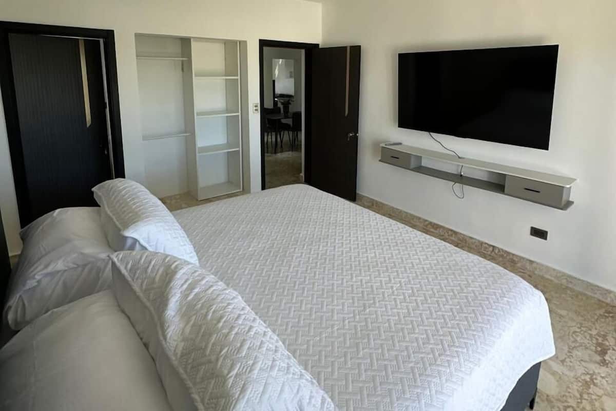A modern hotel room with a large bed, a TV mounted on the wall, and a walk-in closet.